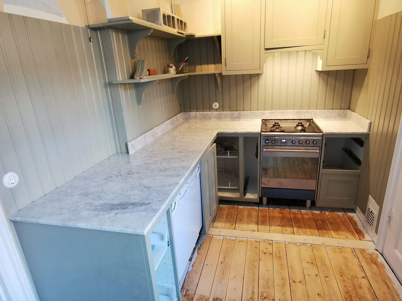Köksbänkskiva i Carrara C, polerad vit marmor med grå ådring, i ett litet kök i Malmö med salviegrön pärlspont, greppfria shakerluckor och en fristående rostfri gasspis.