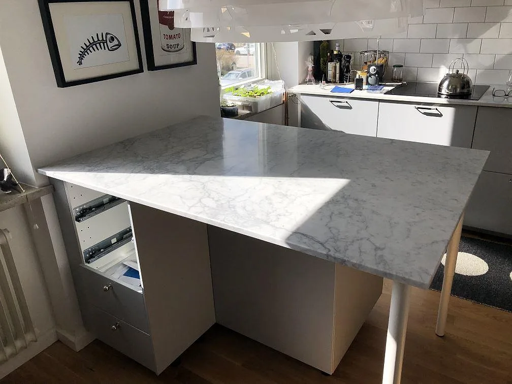 Köksbänkskiva i vit Carrara C marmor, matt, monterad som köksö med frukostbar i ett kök i Malmö, sedd under montering.