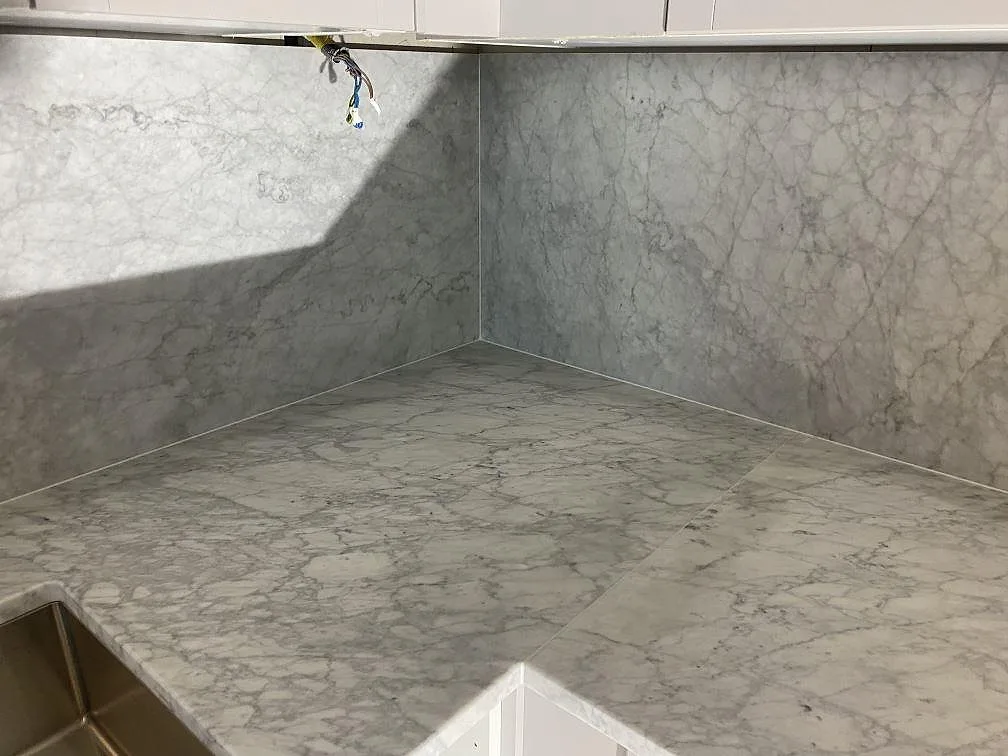 Carrara C marmor bänkskiva och väggbeklädnad i ett hörn med underlimmad rostfri diskho i ett kök i Malmö.