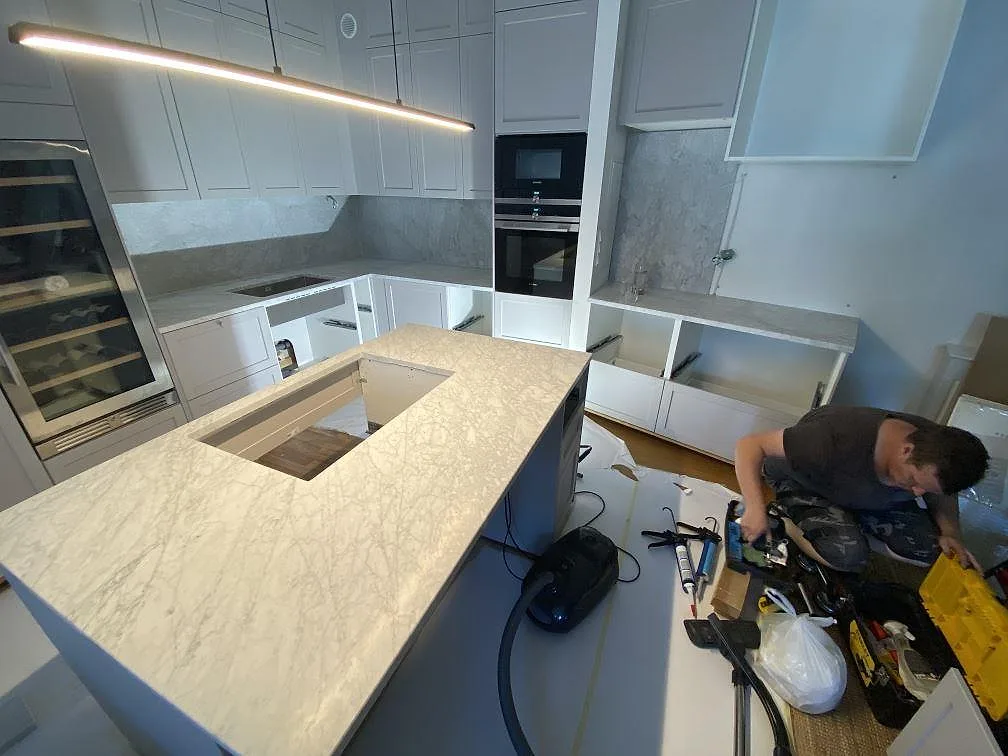 Köksbänkskiva i vit Carrara C marmor, matt, i ett U-format kök med köksö, heltäckande marmorväggbeklädnad och integrerad vinkyl i Malmö.