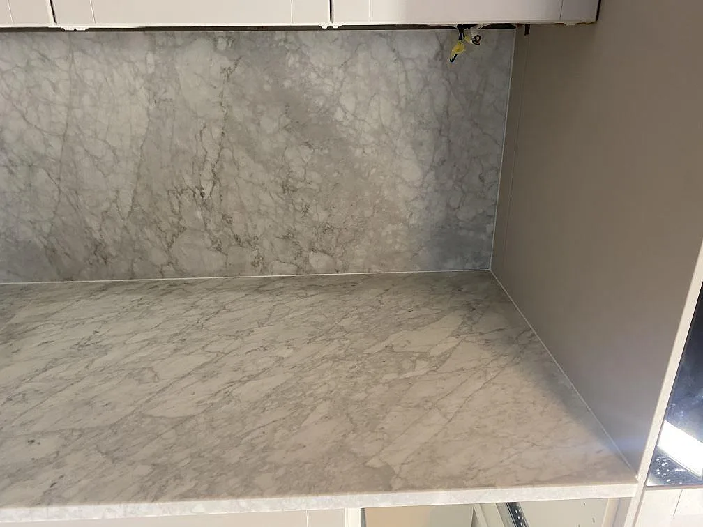 Carrara C marmorbänkskiva med grå ådring och heltäckande marmorvägg bakom i ett kök i Malmö.