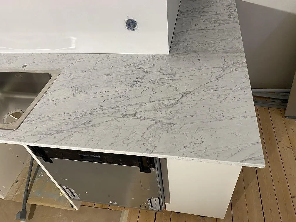 L-formad köksbänkskiva i matt Carrara C marmor med rostfri diskho i ett kök under montering i Malmö.