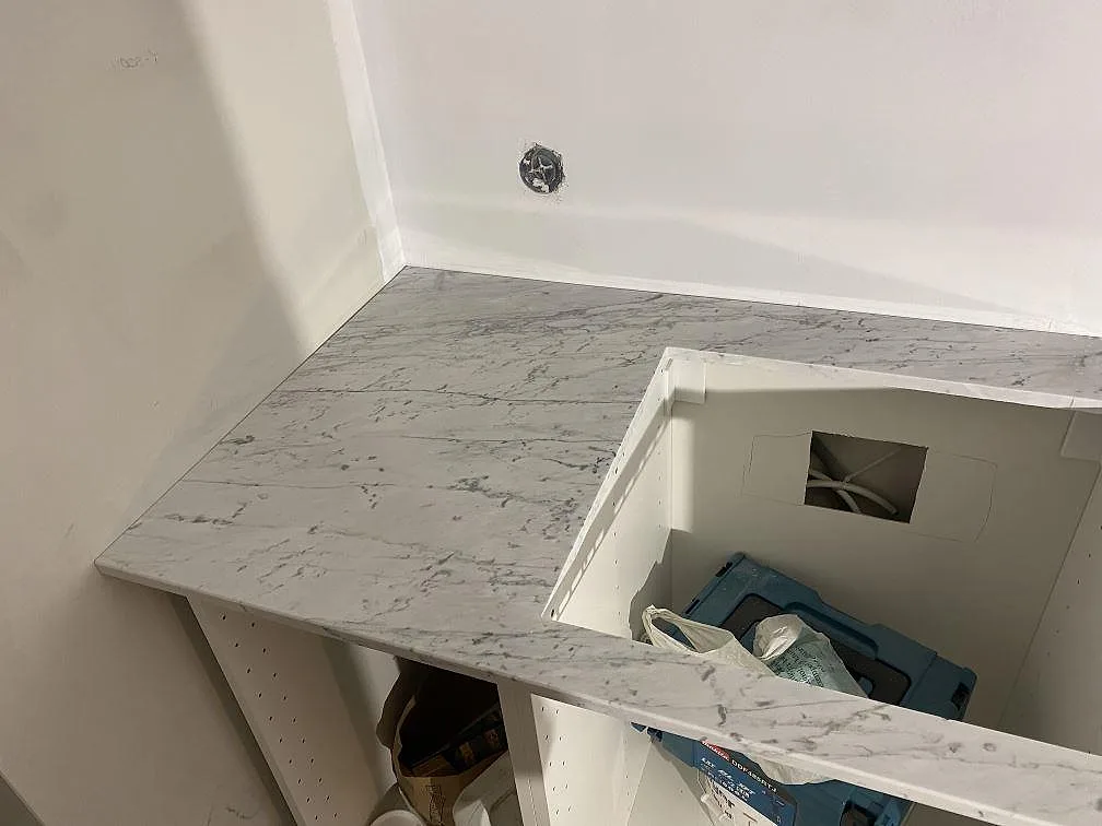 Hörnsektion av en köksbänkskiva i matt Carrara C marmor med grå ådring i ett kök i Malmö.
