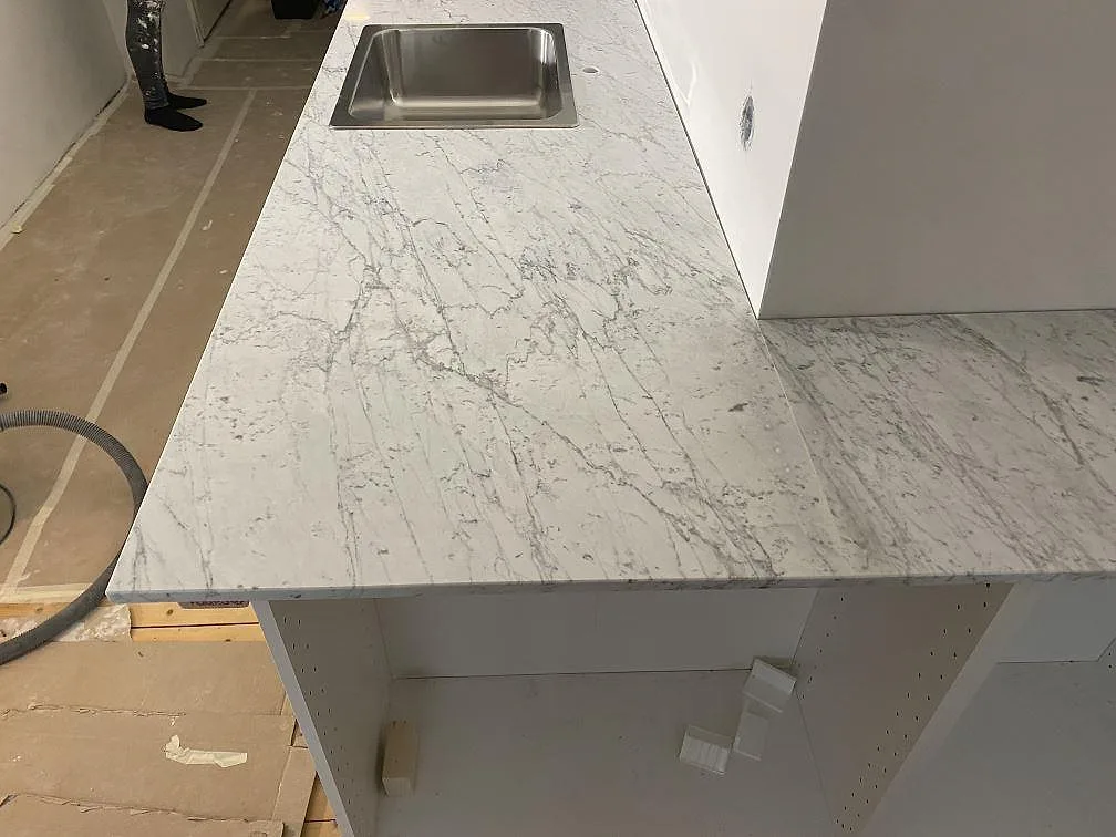 Köksbänkskiva i matt Carrara C marmor med nedfälld rostfri diskho ovanpå stenen i ett kök i Malmö.