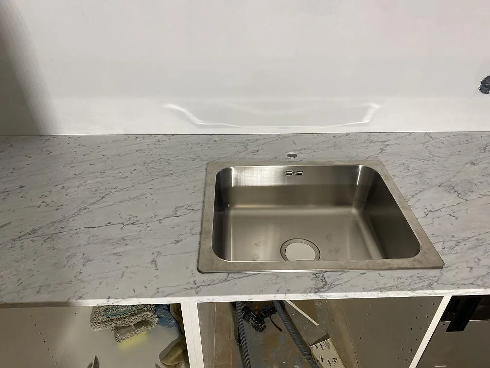 Närbild på nedfälld rostfri diskho ovanpå en köksbänkskiva i matt Carrara C marmor i Malmö.