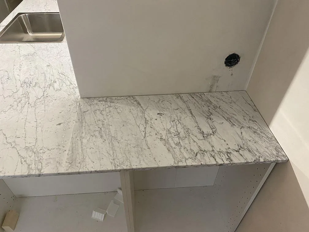 Köksbänkskiva i matt Carrara C marmor med tydlig grå ådring och rostfri diskho i ett kök i Malmö.