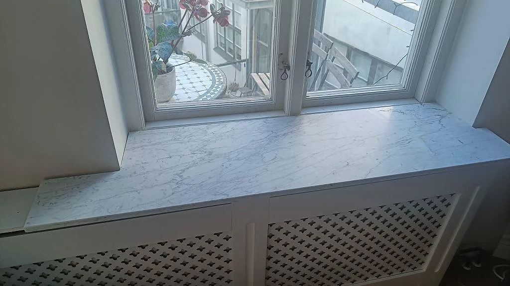 Marmorfönsterbänk i vit Carrara C, matt finish, ovanpå en vit radiatorskärm vid ett fönster i Malmö.