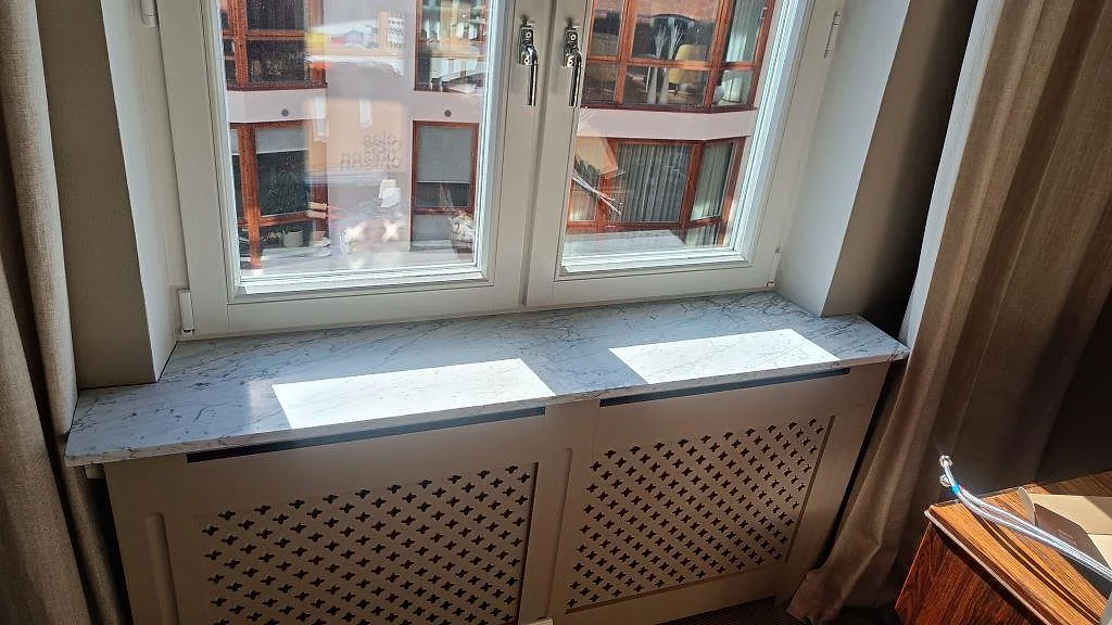 Fönsterbänk i Carrara C-marmor med matt yta och mjuk grå ådring över en målad radiatorskärm i ett rum i Malmö.
