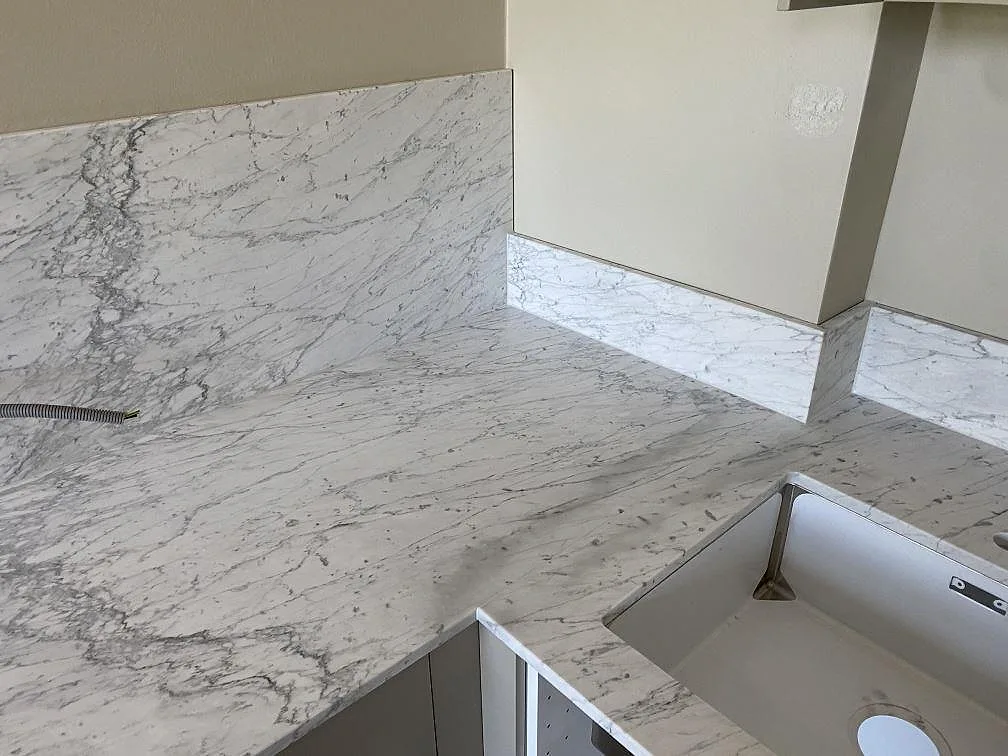 Köksbänkskiva i vit Carrara C marmor med underlimmad diskho och uppvikt stänkkant i ett hörn av ett kök i Malmö.