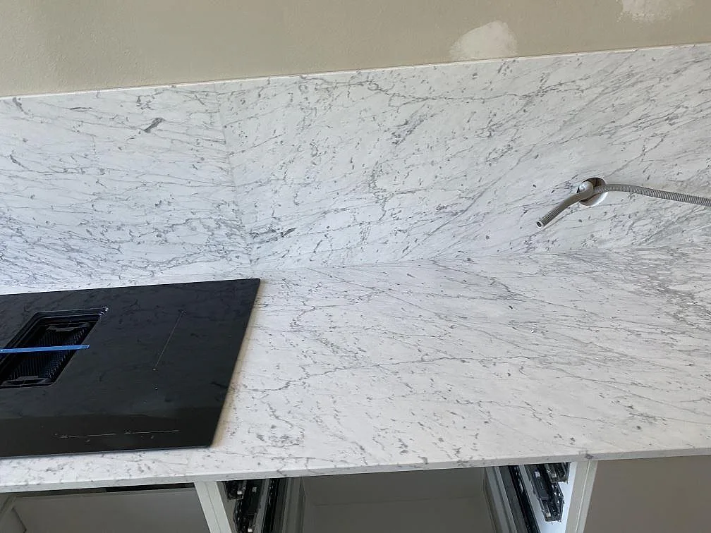 Infälld svart induktionshäll i en matt vit Carrara C marmorbänkskiva med tydlig ådring i ett kök i Malmö.