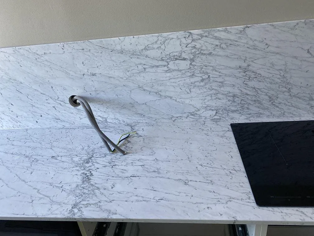 Lång köksbänkskiva i vit Carrara C marmor med infälld svart induktionshäll och grå ådring i ett kök i Malmö.