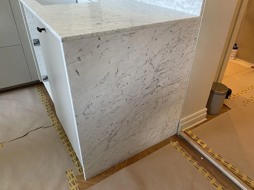 Köksö i vit Carrara C marmor med stensida ner mot golvet och matt ådrig bänkskiva i ett kök i Malmö.