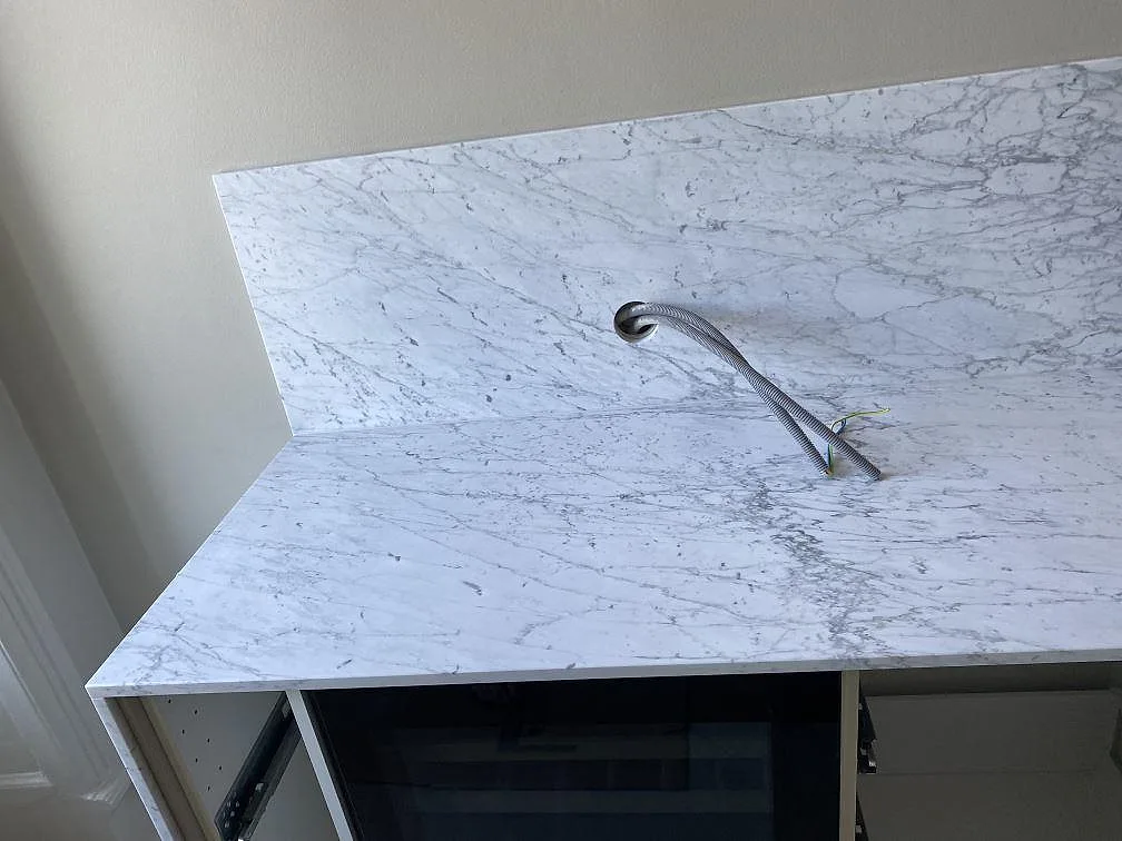 Köksbänkskiva i vit Carrara C marmor med uppvikt stänkkant och synlig ådring under montering i ett kök i Malmö.