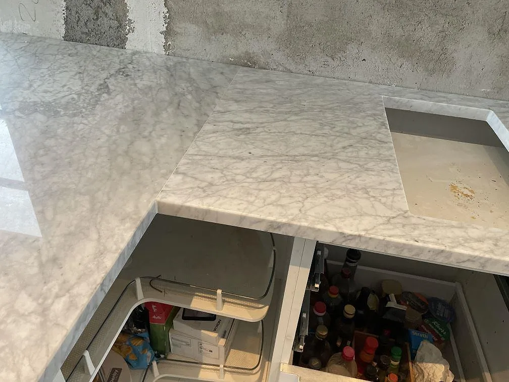 Detalj av Carrara C marmorbänkskiva, polerad, med grå ådring och urtag under montering i Malmö.