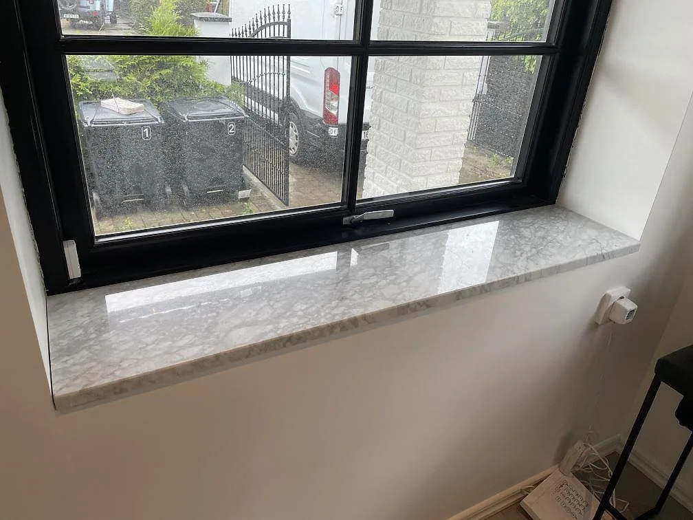 Fönsterbänk i polerad Carrara C marmor under svart spröjsat fönster i Malmö.