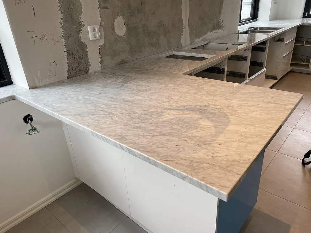 Köksbänkskiva i Carrara C marmor, polerad, med halvö och synliga urtag i ett kök under montering i Malmö.
