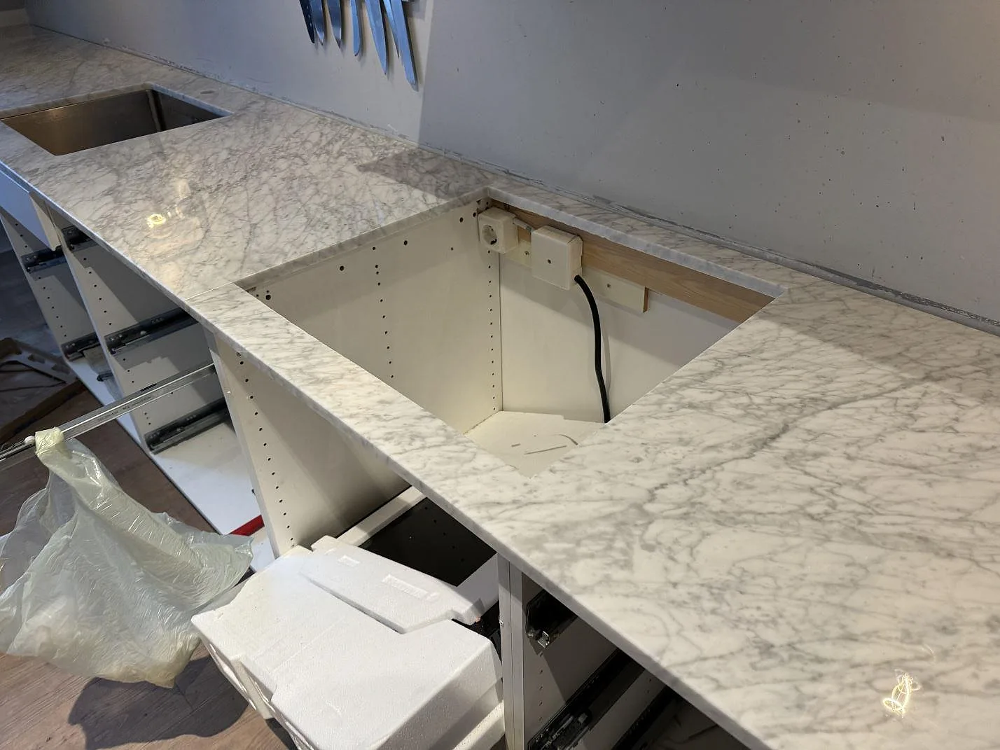 Detalj av polerad Carrara C marmorbänkskiva monterad på vit köksstomme intill högskåp i Malmö.