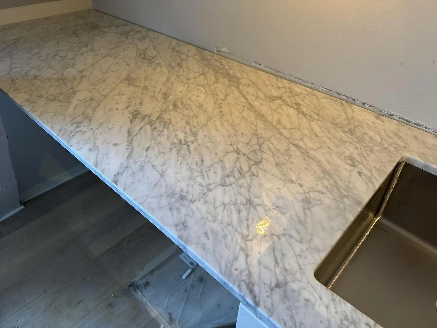 Polerad Carrara C marmorbänkskiva med rostfri diskho, kranhål och vit köksstomme under montering i Malmö.
