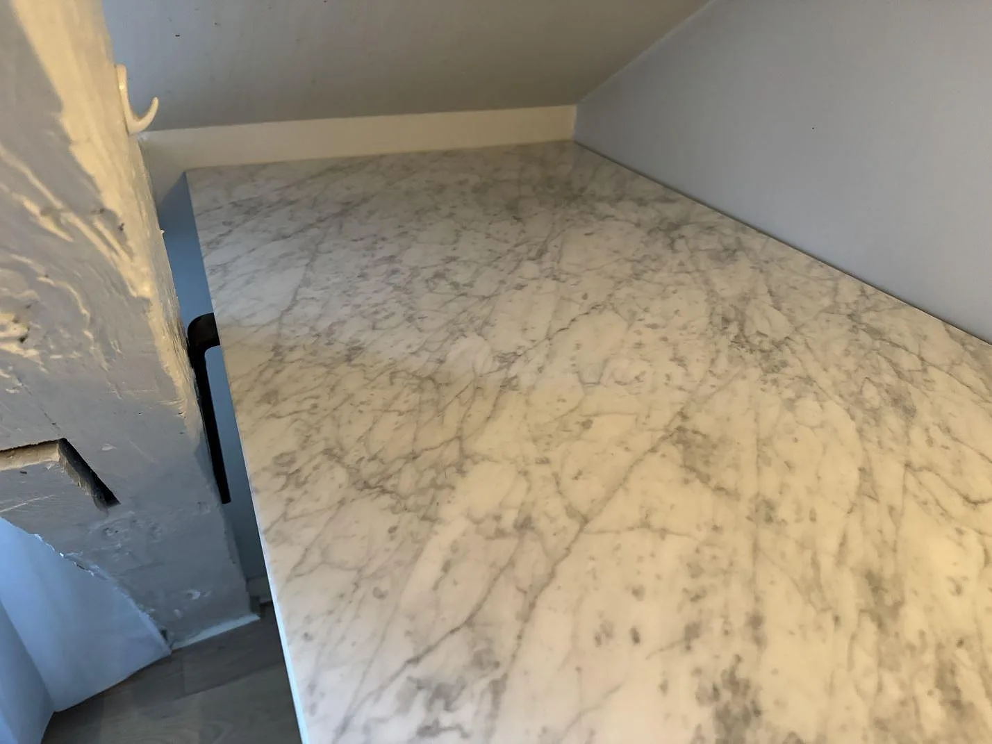 Carrara C marmorbänkskiva med stort rektangulärt hälluttag och öppen vit stomme under montering i Malmö.