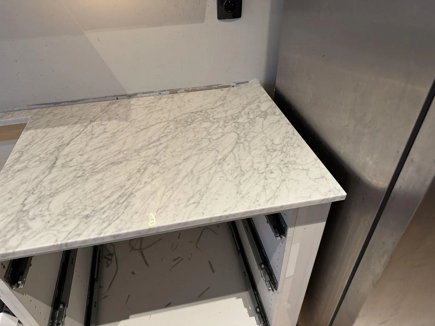 Smal bänkyta i polerad Carrara C marmor med tät grå ådring monterad i köksnisch i Malmö.