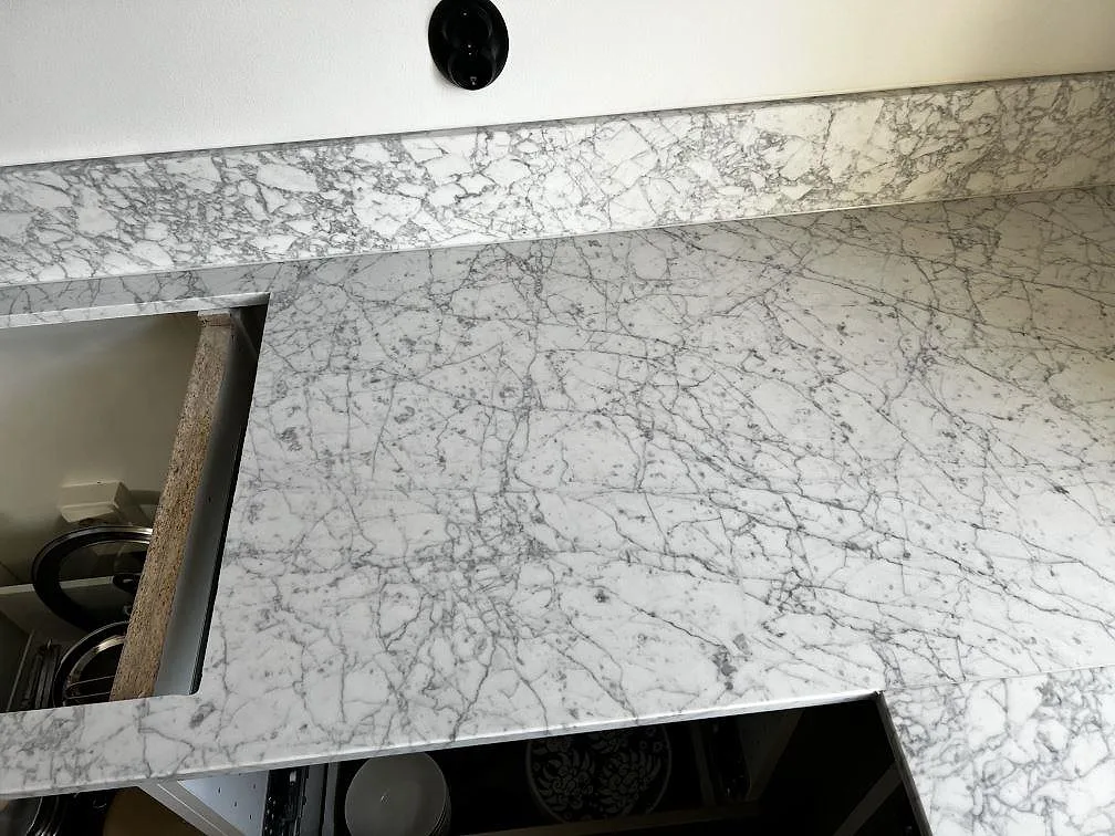 Detalj av matt Carrara C marmor med grå ådring, stänkkant och hälluttag i ett kök i Malmö.