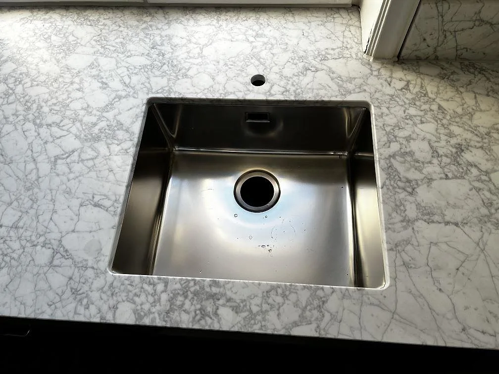 Närbild på underlimmad rostfri diskho i en köksbänkskiva av matt Carrara C marmor i Malmö.