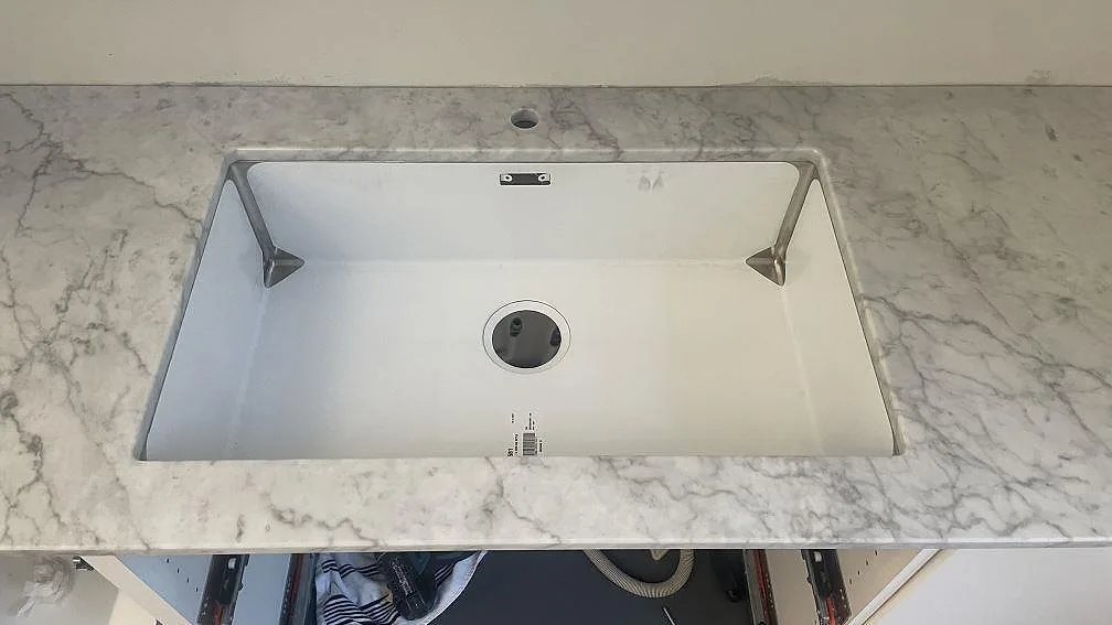 Närbild på underlimmad rostfri diskho i polerad Carrara C marmorbänkskiva i Malmö.