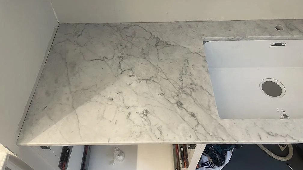 Vänster sida av köksbänkskiva i polerad Carrara C marmor med diskho och öppna stommar i Malmö.
