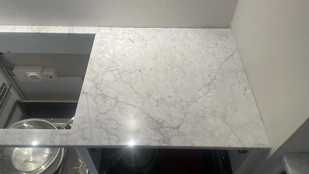 Blankpolerad Carrara C marmorbänkskiva med hällöppning och ugn i ett vitt Malmö-kök.