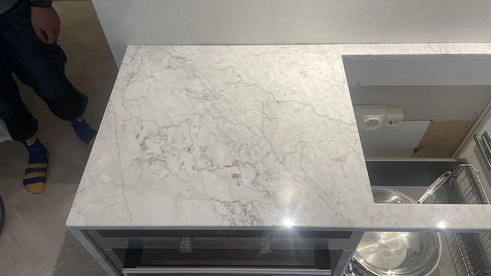 Polerad marmorbänkskiva i Carrara C med hälluttag och öppna vita stommar under montering i Malmö.