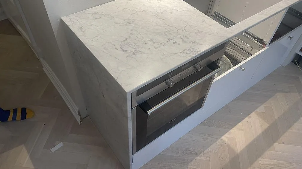 Polerad Carrara C bänkskiva i marmor vid ugn och hällöppning i ett kök under montering i Malmö.