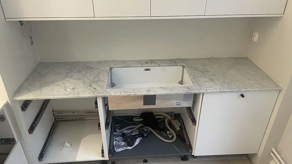 Köksbänkskiva i Carrara C marmor, polerad, med underlimmad rostfri diskho i ett vitt kök i Malmö.