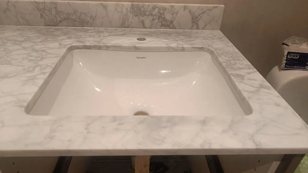 Detaljbild av underlimmat vitt tvättställ i en matt Carrara C marmorbänkskiva med stänkkant i Malmö.