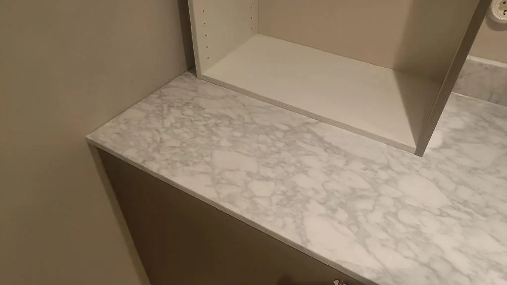 Sidoyta i matt Carrara C marmor över träinredning i ett badrum, med tydlig grå ådring i Malmö.