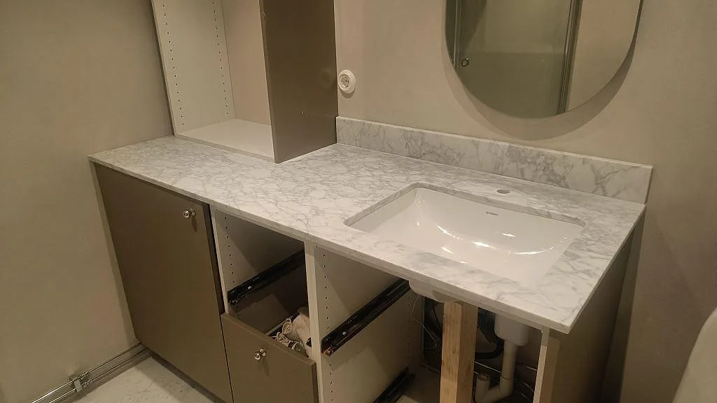 Badrumsbänkskiva i matt Carrara C marmor med vitt underlimmat tvättställ och uppvikt stänkkant i Malmö.