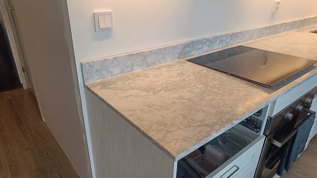 Närbild på matt Carrara C bänkskiva i kök i Malmö med svart häll, ljus ådring och stänkkant i samma marmor.