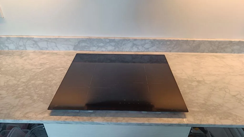 Frontal detalj av svart häll infälld i matt Carrara C marmor med matchande stänkkant i ett kök i Malmö.
