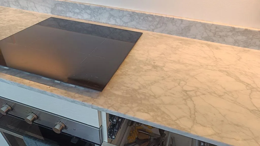 Sned närbild på matt Carrara C köksbänkskiva med svart häll, stänkkant och grå marmorådring i Malmö.