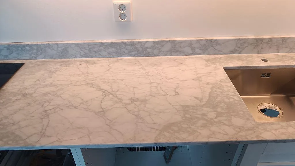 Carrara C bänkskiva i matt marmor med rostfri underlimmad diskho, tapputtag och låg stänkkant i ett kök i Malmö.