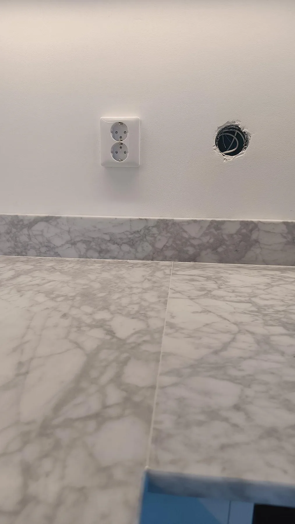 Detalj av matt Carrara C bänkskiva och stänkkant vid vägguttag i ett kök under montering i Malmö.