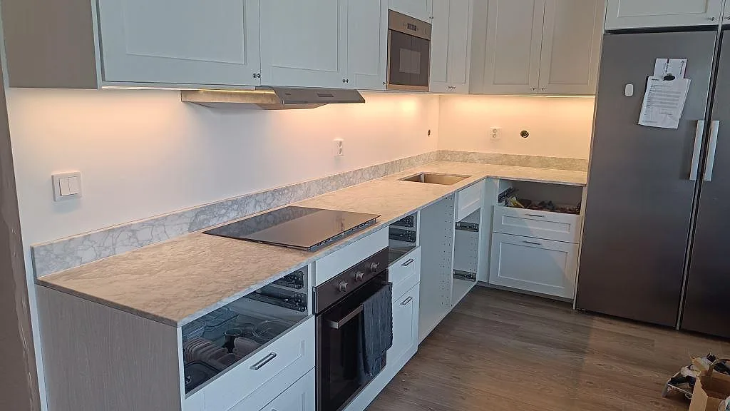 L-format kök i Malmö med matt köksbänkskiva i Carrara C marmor, låg stänkkant, svart häll och rostfri diskho.