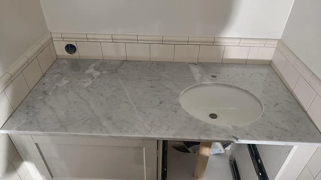 Badrumsbänk i polerad Carrara C marmor med rund vit tvättställsskål och kaklad nisch i Malmö.