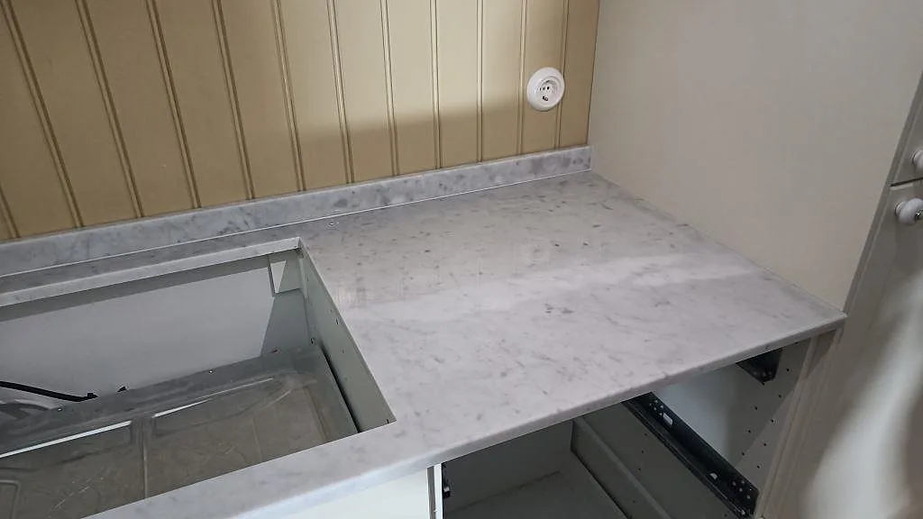 Bänkskiva i polerad Carrara C marmor med låg stenkant och rektangulär öppning i ett rum i Malmö.