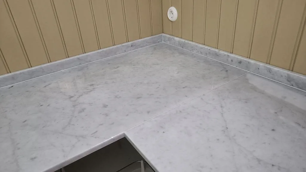 Närbild på polerad Carrara C marmor över en hörnyta med låg uppvikt stenkant och synlig ådring i Malmö.