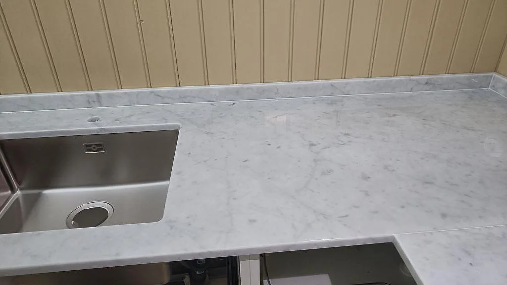 Polerad Carrara C marmor som arbetsyta med synlig rostfri ho och låg stenkant i Malmö.