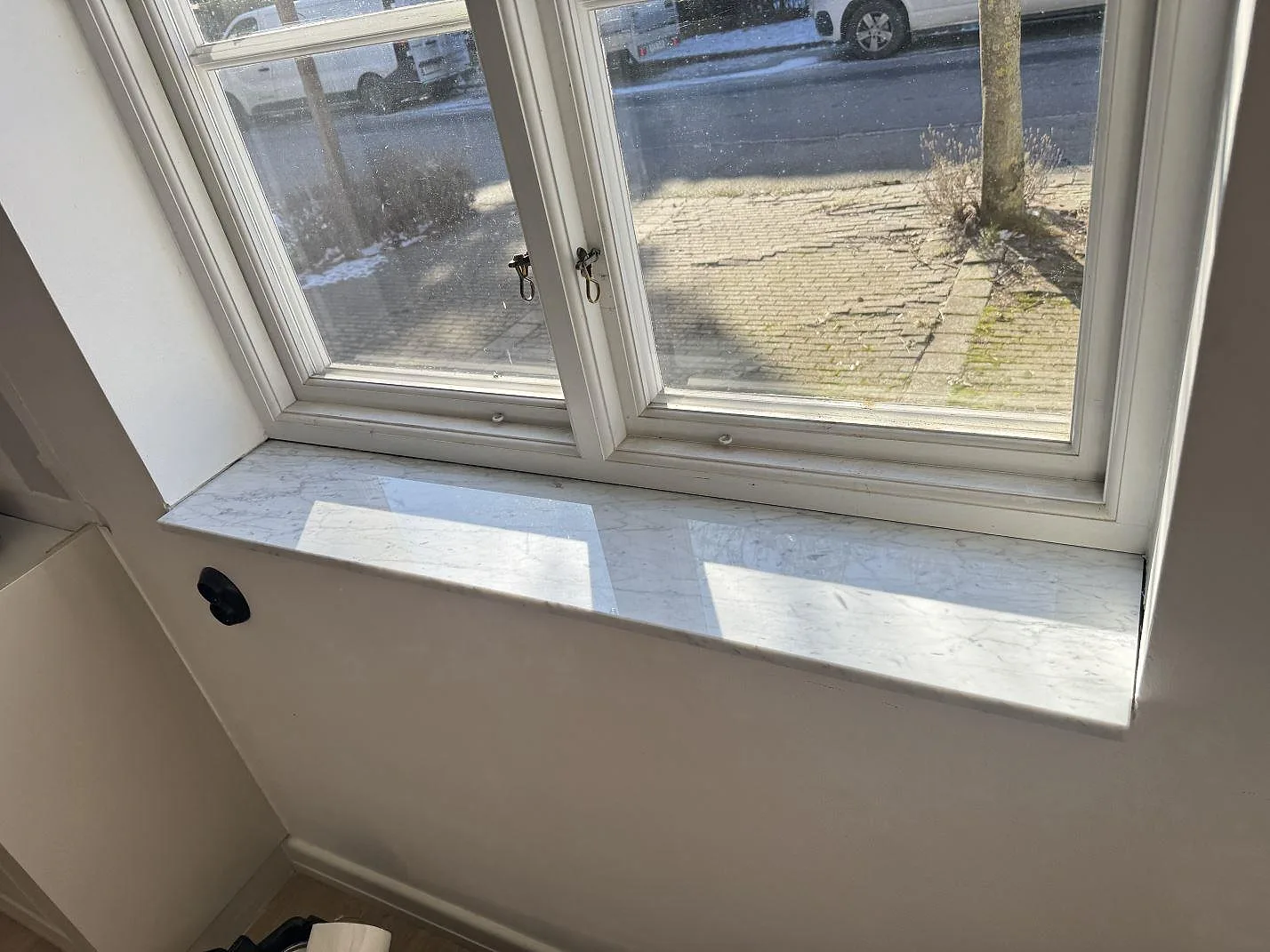 Lång fönsterbänk i polerad Carrara C-marmor med blank yta och gatuljus genom fönstret i Malmö.