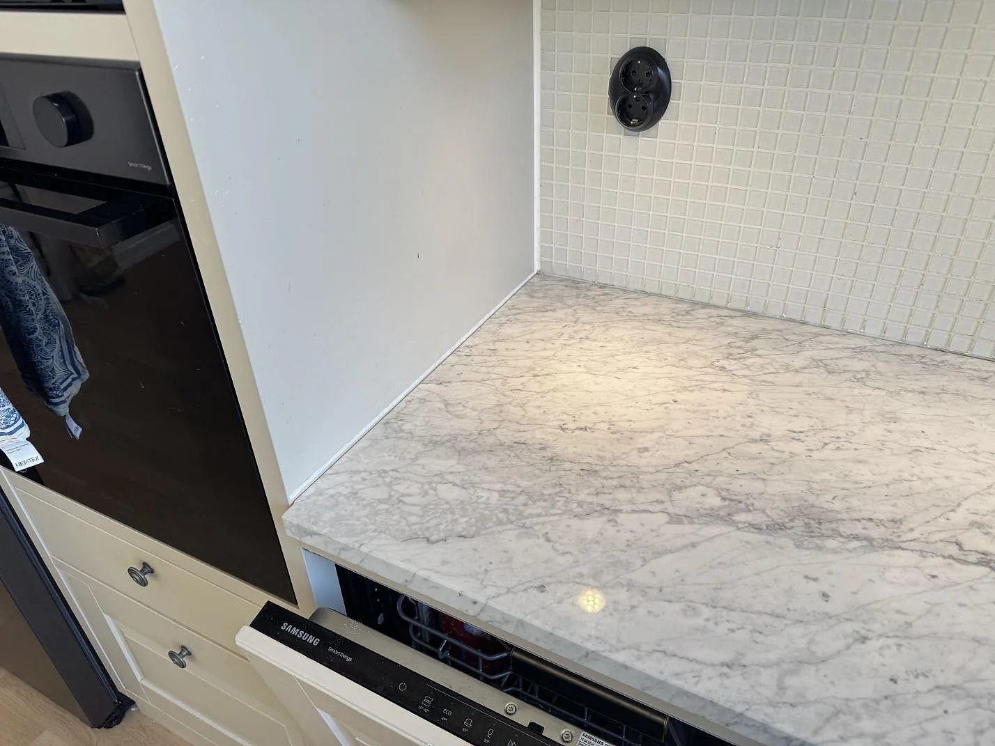 Polerad köksbänkskiva i Carrara C-marmor med synlig grå ådring, ugn och diskmaskin i ett kök i Malmö.