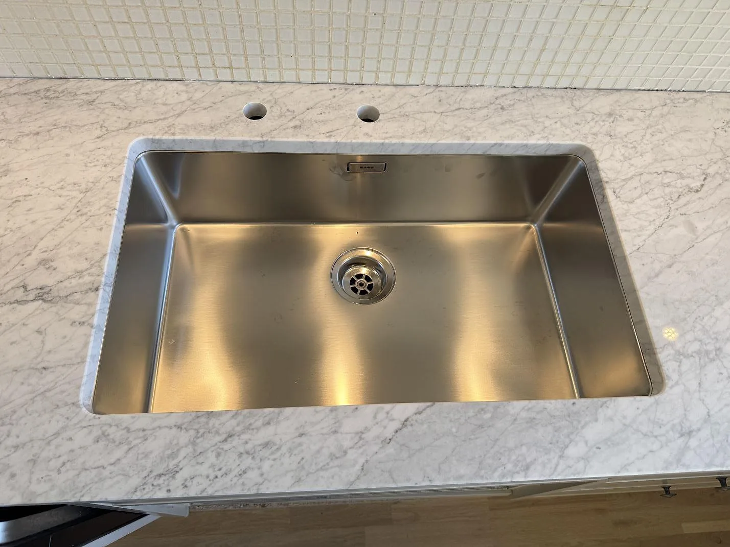 Närbild på rostfri diskho i en polerad köksbänkskiva av Carrara C-marmor i Malmö.