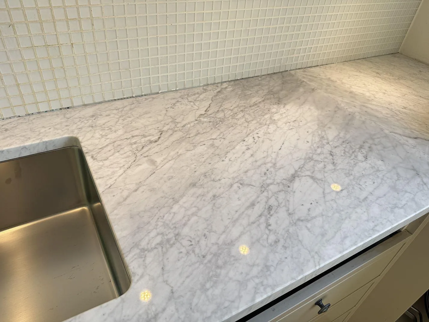 Detalj av Carrara C-marmor som köksbänkskiva med blank polerad yta och grå ådring intill diskhon i Malmö.