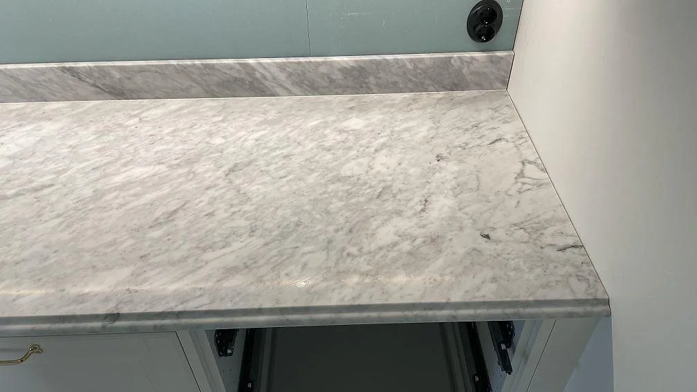 Närbild på matt Carrara C marmor med grå ådring, framkant och uppvikt stänkkant i ett kök i Malmö.